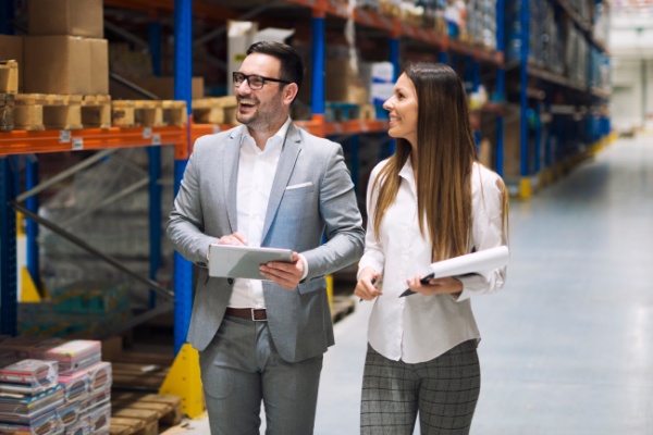 Man and woman, smiling and walking through a warehouse.
