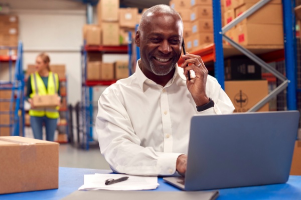 Man smiling working on his laptop and talking on his phone.